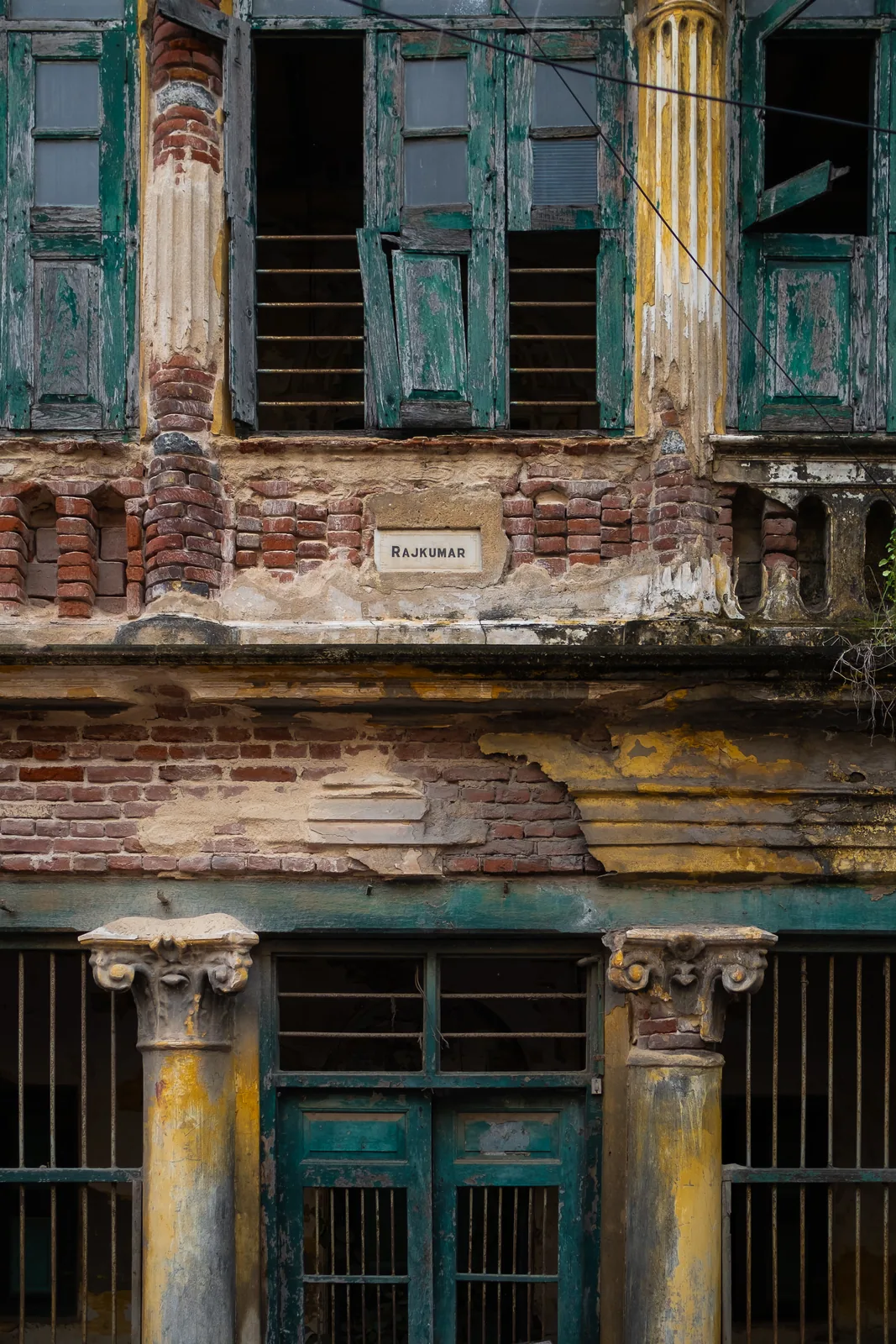 The full height of the old façade, louvres above and columns below, stacked into a vertical study in teal, brick and ochre.