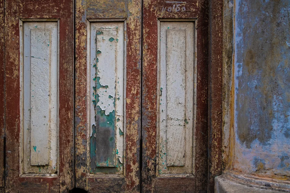 Maroon frames and white panels flaking away in long strips beside a wall washed in blue.