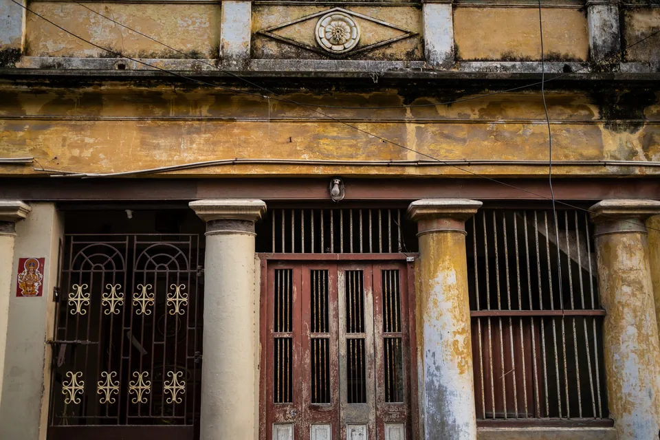 Three bays of cast-iron grilles between round columns, under a cornice of crumbling ochre.