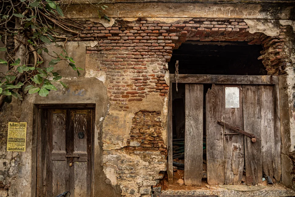 A crumbling brick wall frames two doors, one patched and one barely standing.