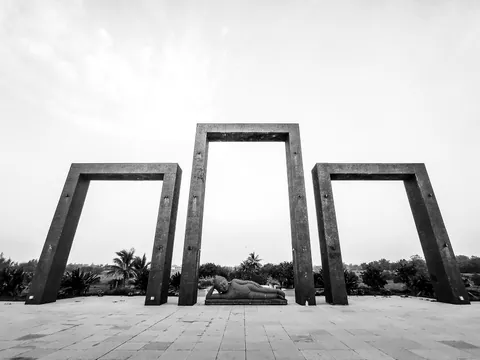Three monumental stone frames stand open to a pale sky, a reclining figure resting between them.