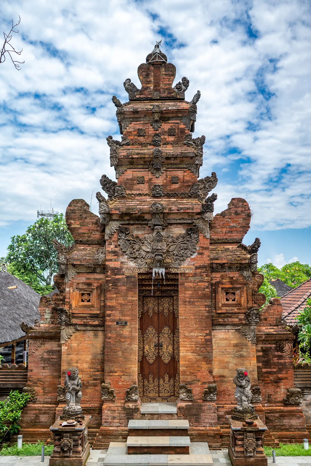 A red-brick temple gate with carved stone tiers rises into a sky of tumbling cloud.