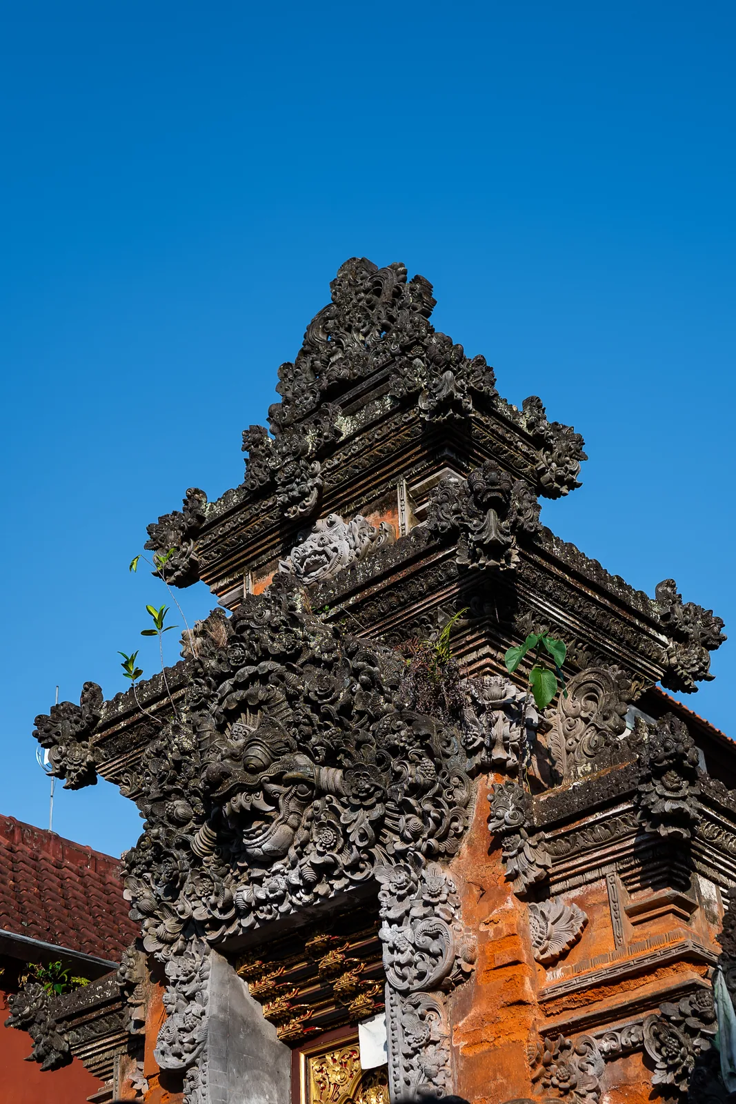 The carved stone tiers and orange brick of a temple gate against a clean blue sky.