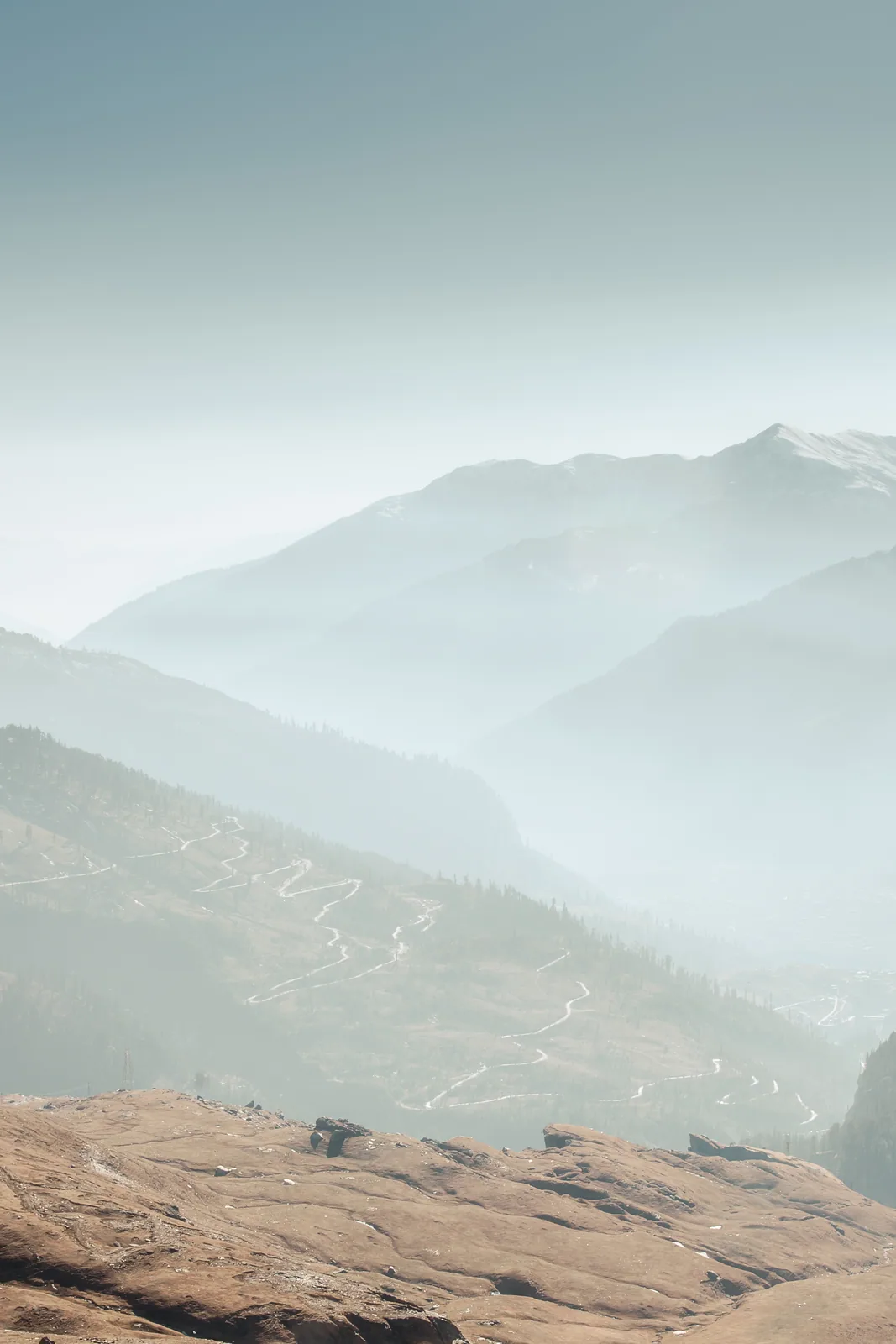 Ridge after ridge of pale blue fades into mist above a sunlit slope.