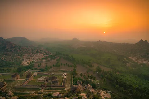 The sun sinks into an orange haze over Hampi's boulder country and the ruins of a great temple complex.