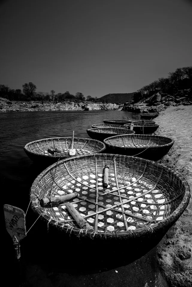 Round woven coracles rest in a row on a rocky riverbank.