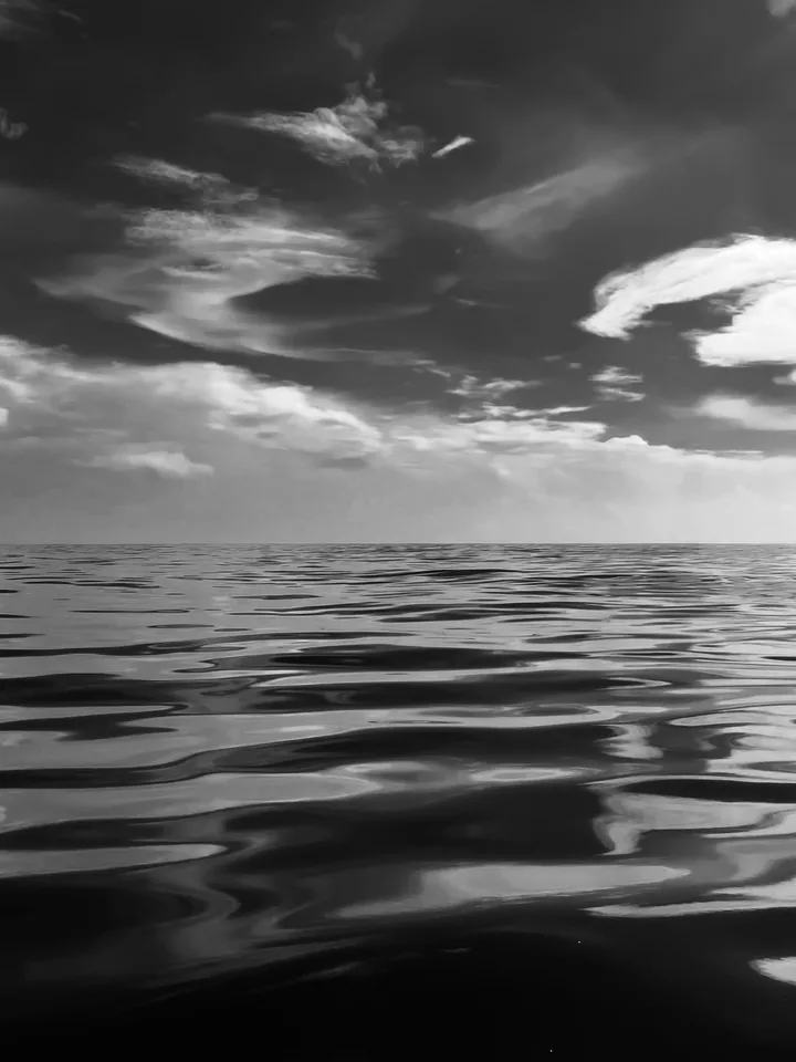 Ripples gleam across a dark sea beneath streaks of bright cloud.